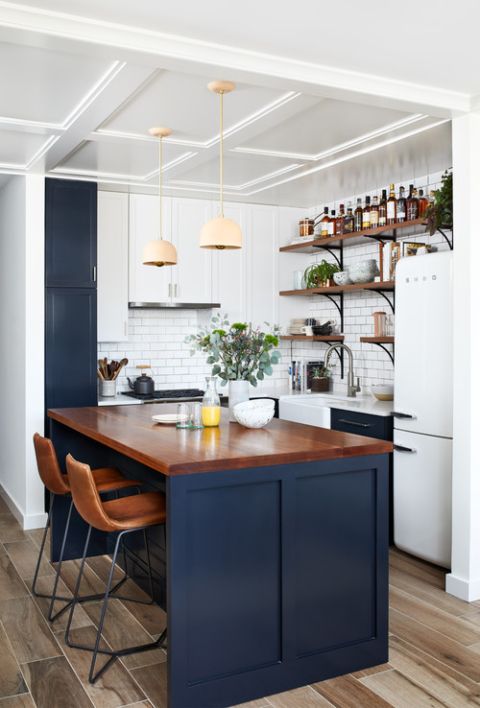 A small farmhouse kitchen in white and navy, featuring a kitchen island with stained countertops, pendant lamps and a subway tile backsplash