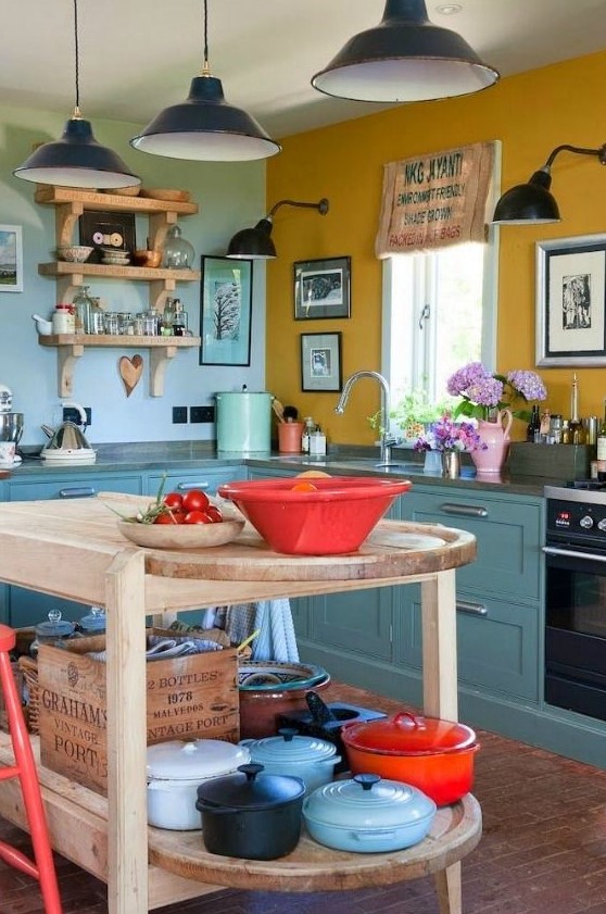 a bold, eclectic kitchen with a mustard yellow and blue wall, teal cabinets, gray stone countertops, open shelving and black pendant lamps