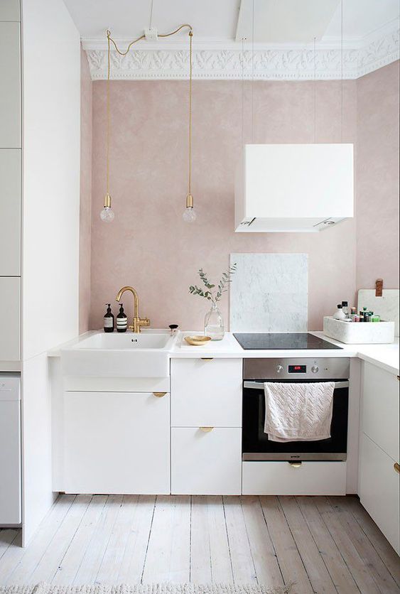 a small and calm modern kitchen with blush walls, white cabinets with gold handles, hanging lamps and a white extractor hood