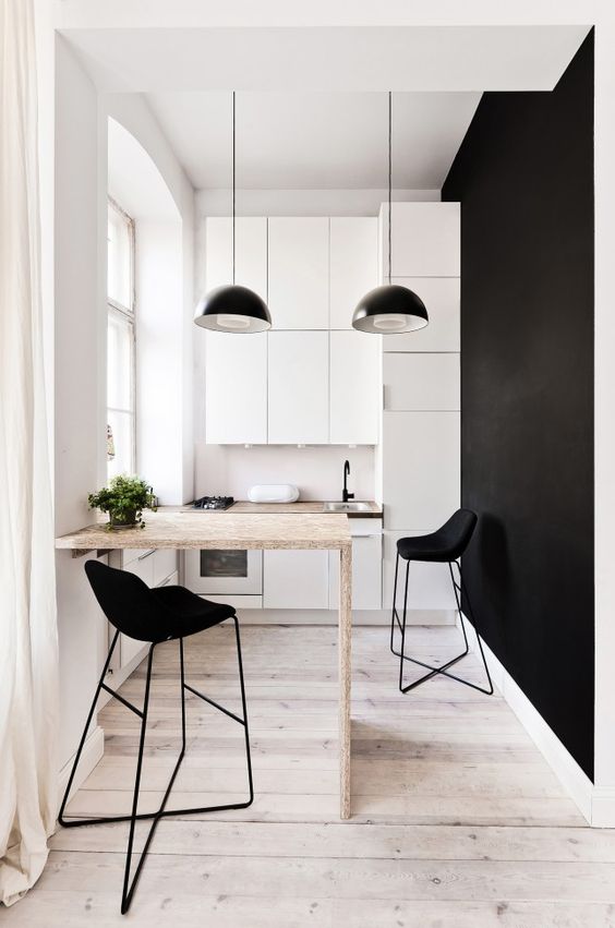 a minimalist, monochromatic kitchen with white sleek cabinets, black pendant lamps, a plywood countertop, black stools and a black statement wall