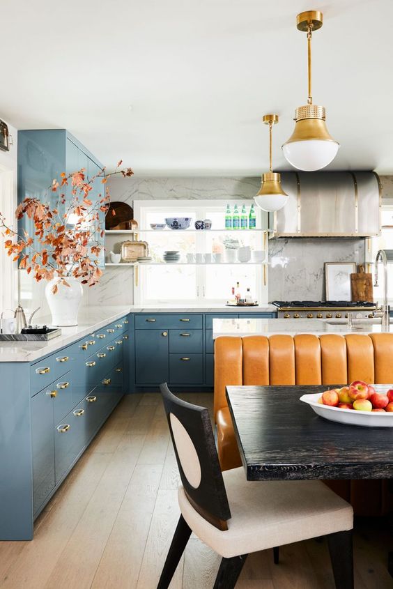 a bright, eclectic kitchen with dusty blue cabinets, white marble countertops, an island, an amber leather sofa, and pendant lamps