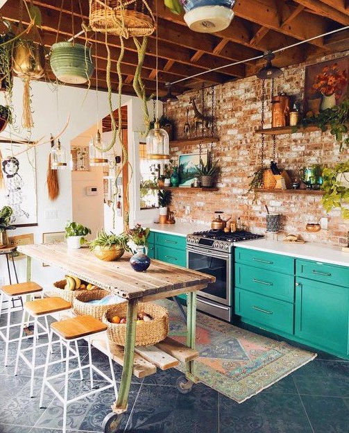 a striking, eclectic kitchen with emerald green cabinets, white countertops, a stainless steel stove, a rolling table and stool, and lots of plants