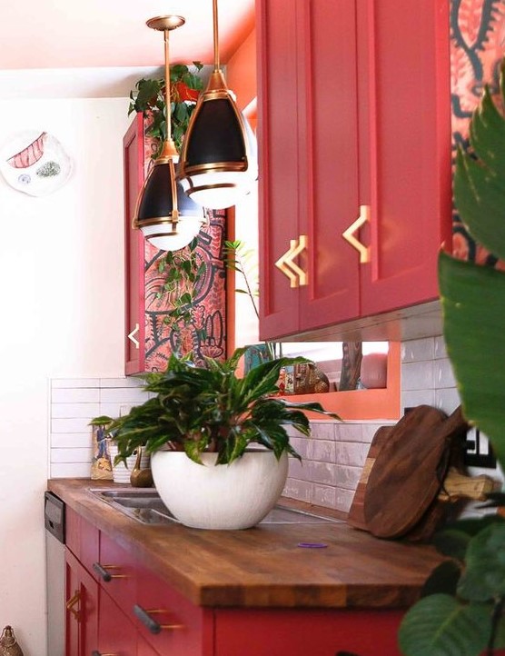 a chic maximalist kitchen with red cabinets, butcher block countertops, retro pendant lamps and lots of potted plants