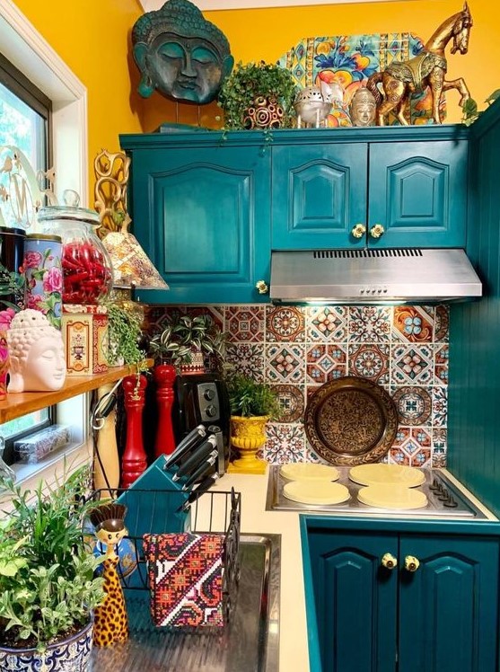 a colorful maximalist kitchen with mustard-colored walls, teal cabinets, colorful tiles on the back wall and lots of accessories and potted plants