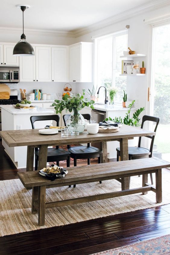 a cool, eclectic kitchen with white cabinets, a white backsplash, a rustic dining set with benches, black chairs and a black pendant lamp