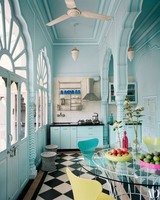 a light blue Moroccan-style kitchen with black countertops, checkered floor, a round glass table, yellow and blue chairs