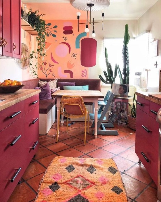 a maximalist kitchen with an orange wall, fuchsia cabinets, a mid-century modern chandelier, and statement textiles