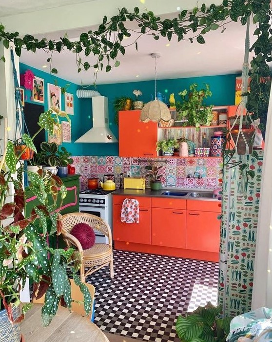 A maximalist space with emerald green walls, red cabinets, a colorful tile backsplash and artwork, as well as a tile floor and plants