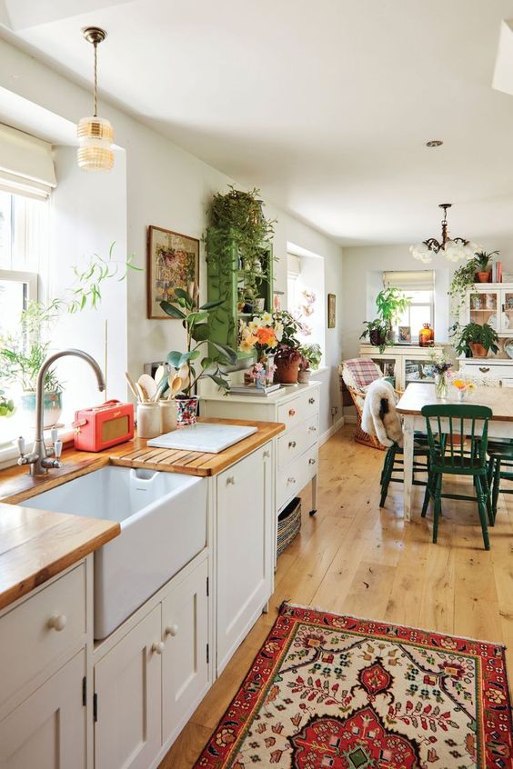 a lovely, eclectic kitchen with neutral cabinets, butcher block countertops, a green storage cabinet, and a dining table with mismatched chairs