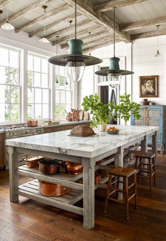 an eclectic kitchen with a blue shabby chic buffet, a large table that serves as a kitchen island, stained cabinets and stools, and hanging lamps