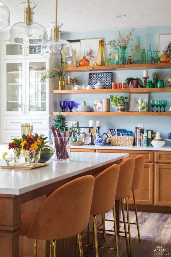 an eclectic kitchen with amber cabinets and shelves, a kitchen island that doubles as a table, amber stools and pendant lamps