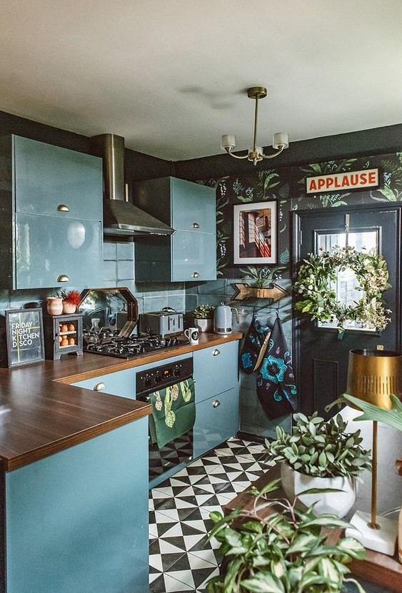 an eclectic kitchen with black walls, blue sleek cabinets, butcher block countertops, a black and white tile floor, and potted plants