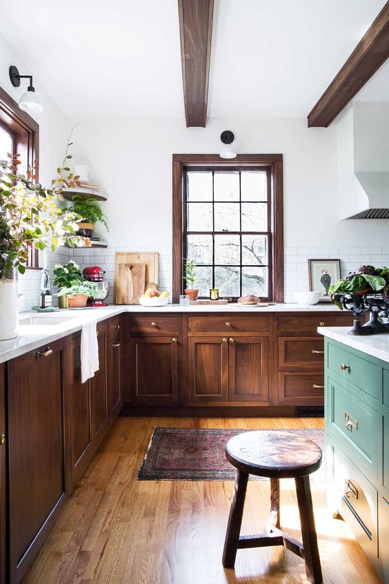 an eclectic kitchen with dark-stained cabinets, a green island, dark wood beams and a stool, as well as potted plants