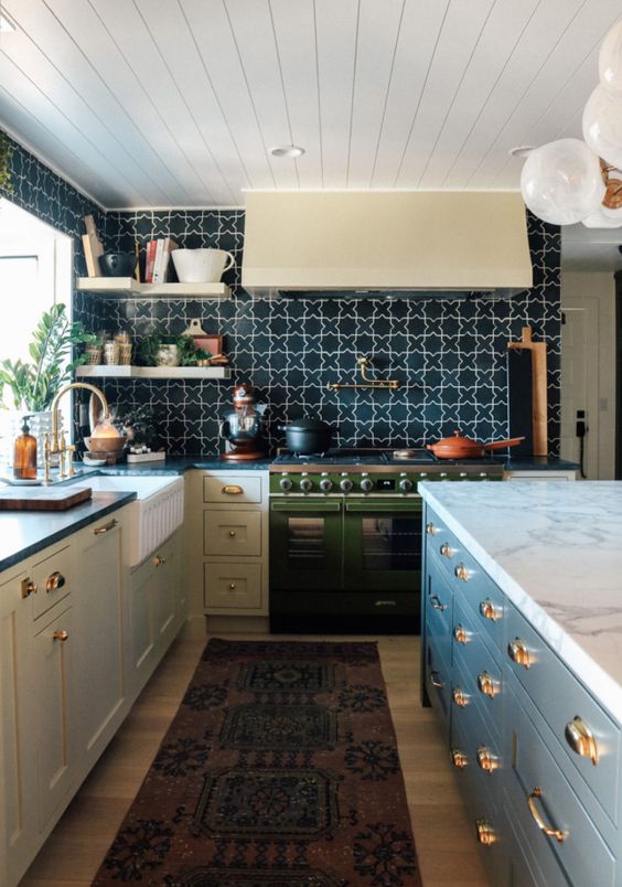 an eclectic kitchen with gray cabinets, a green stove, a black-and-white printed tile backsplash, and open corner shelves