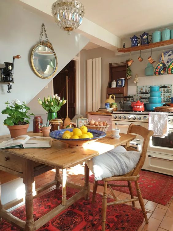 an eclectic kitchen with neutral and pink cabinets, open shelving, a vintage wooden table and chair, and a crystal pendant lamp