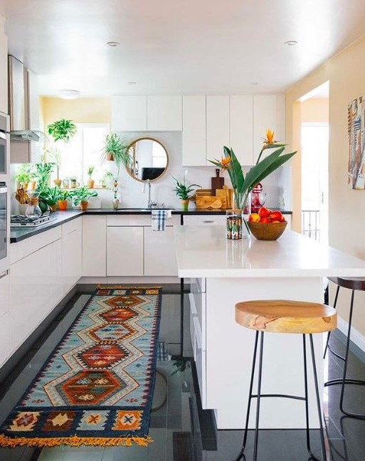 an eclectic kitchen with sleek white cabinets, black stone countertops, a statement rug, potted plants and stools