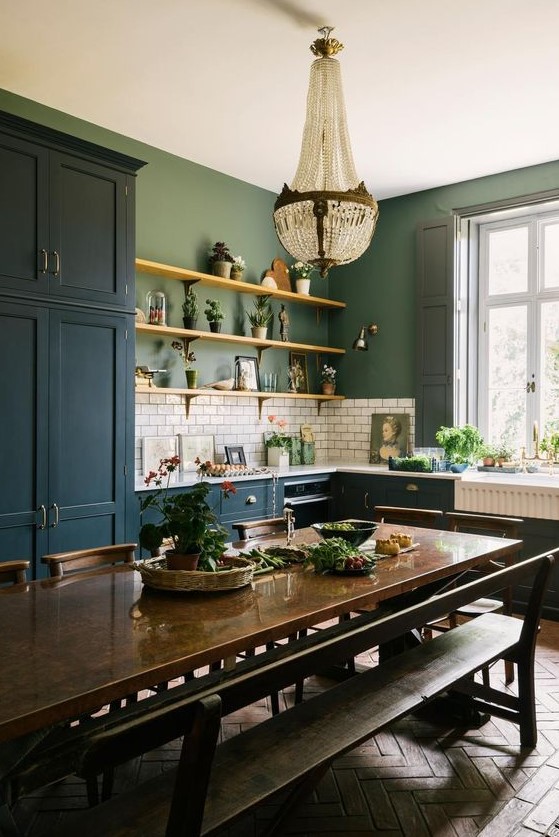an eclectic kitchen with teal cabinets, green walls, white subway tiles, a crystal chandelier, a dark stained table, and benches and chairs