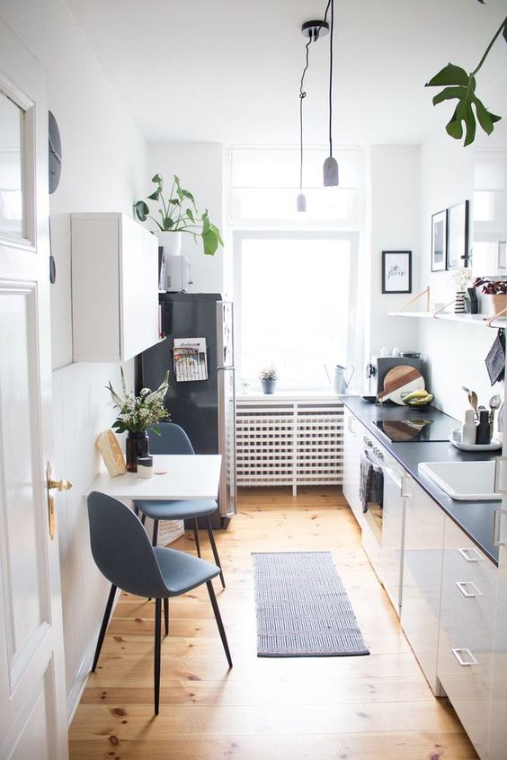 a chic white kitchen with black countertops, open shelves, a folding table and gray chairs, and plants