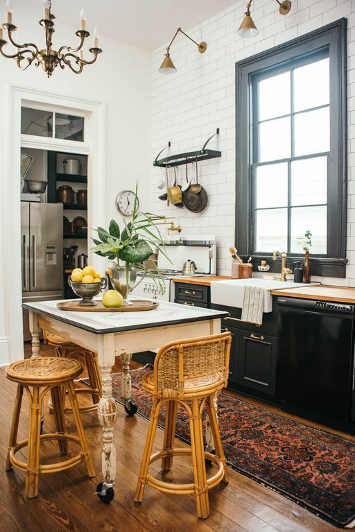 A chic kitchen with black cabinets and neutral countertops, a shabby-chic style table, vintage rattan chairs and industrial lamps