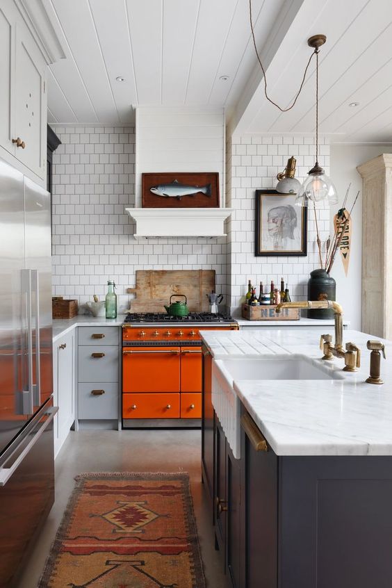 a bright, eclectic kitchen with an orange stove, navy and gray cabinets, white stone countertops and memorable artwork