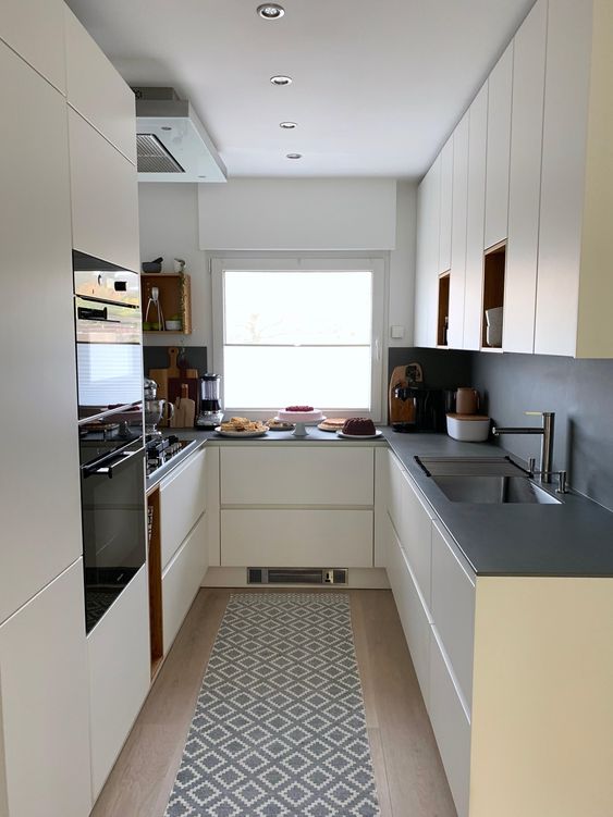 a creamy, elegant kitchen with a gray splashback and worktops, built-in appliances and a window with a view