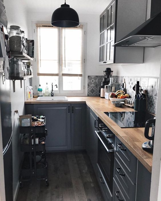 a graphite gray kitchen with butcher block countertops, a black cart and black pendant light, and gray printed tiles