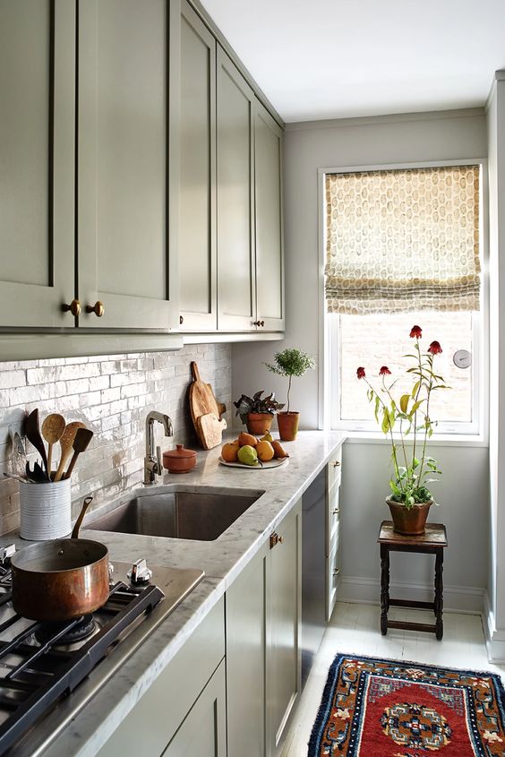 A green single-wall kitchen with stone countertops and a tiled backsplash and some printed textiles is chic