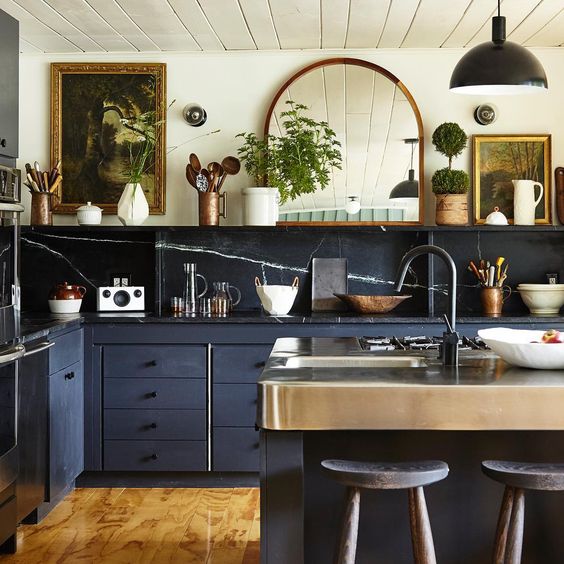 A beautiful, eclectic kitchen combining stone splashbacks and countertops, navy blue cabinets, vintage artwork and a mirror