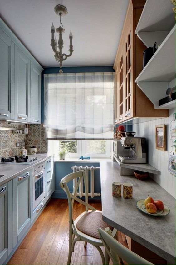 a light blue kitchen with blue walls, stained and blue cabinets, concrete countertops and a vintage pendant lamp