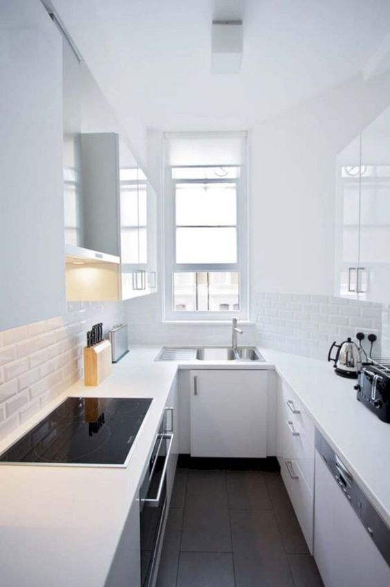 A minimalist, all-white kitchen with thin white tiles, a window and black built-in appliances is pure chic