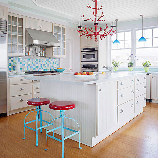 A white farmhouse kitchen jazzed up with a glass tile backsplash, two ottomans and a unique red chandelier