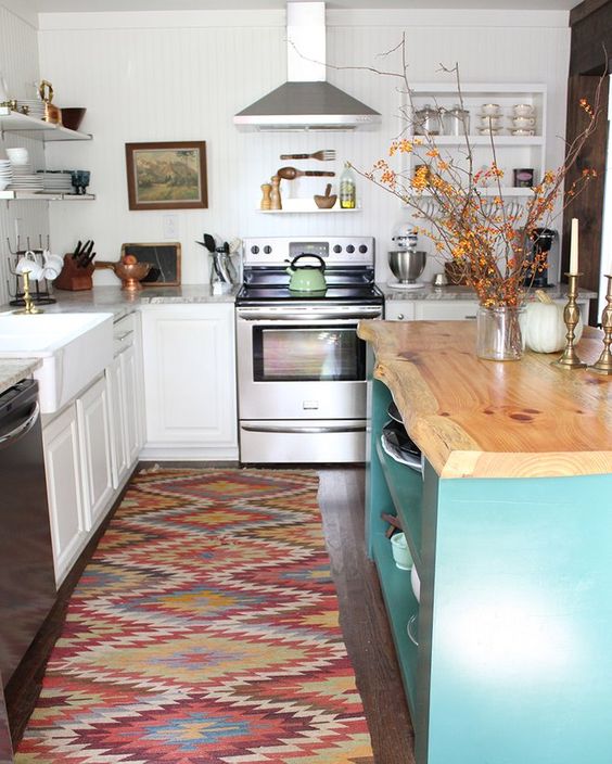 a white traditional kitchen, a colorful boho rug, a blue kitchen island with a live edge wooden countertop