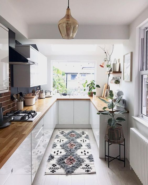 a pretty little kitchen with white cabinets, kitchen countertops, potted plants and a printed rug
