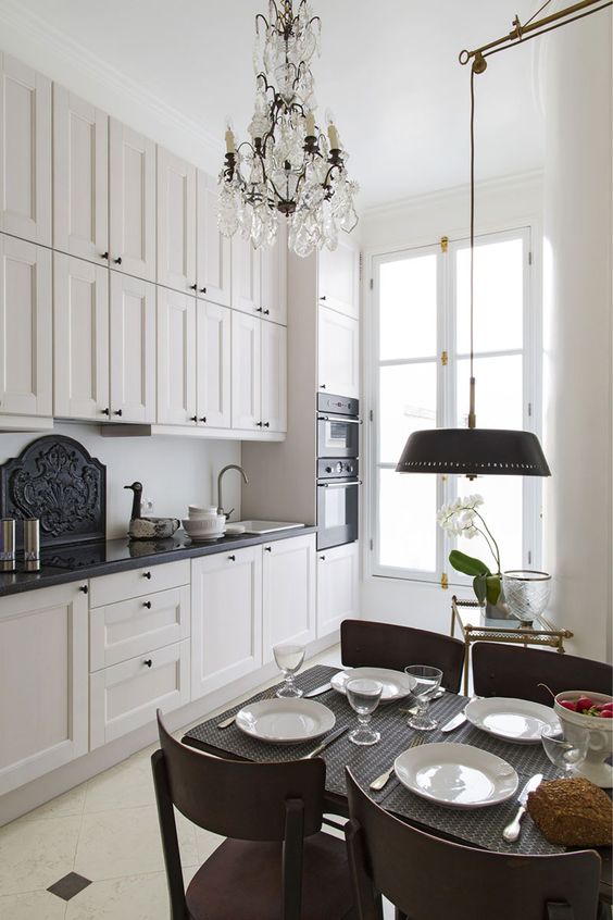 a small and chic French-style kitchen with black countertops, crystal chandeliers and a small dining area with an additional lamp