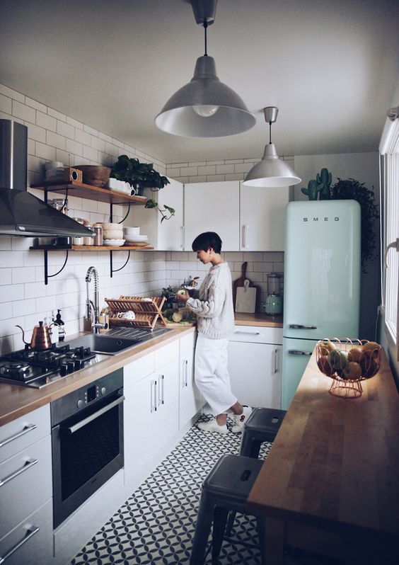 a small and cozy Scandinavian kitchen with white cabinets, butcher block countertops, a mint refrigerator and a white tile backsplash
