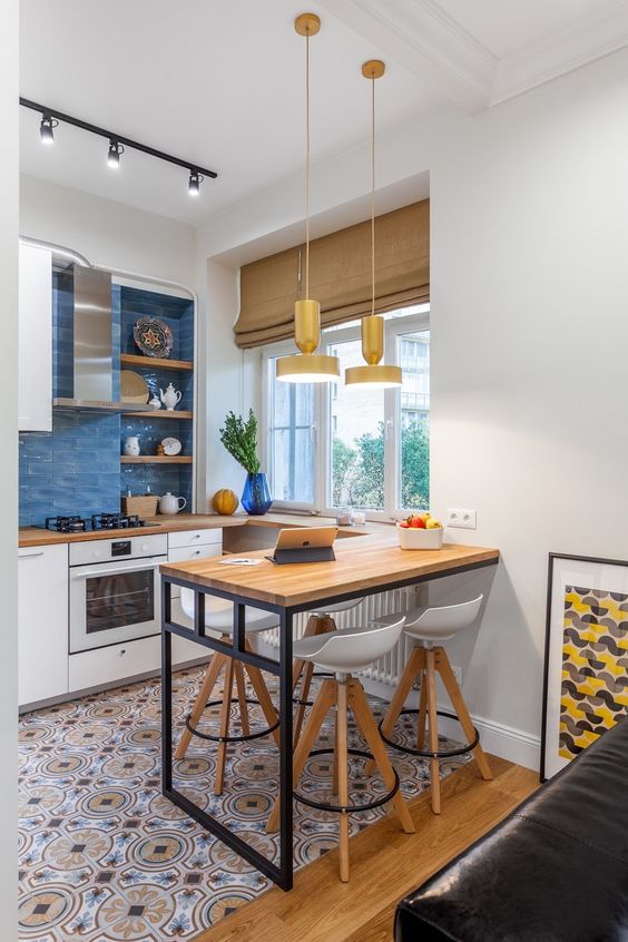 a small modern kitchen with white cabinets, printed tiles on the floor, butcher block countertops and a wall-mounted table