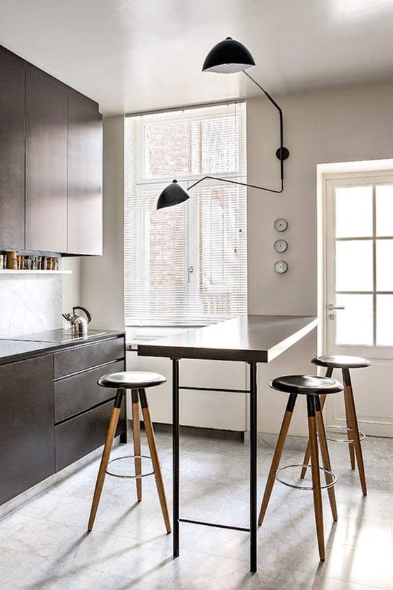 a small kitchen with sleek brown cabinets, a high bar countertop and tall stools, and a cool wall light
