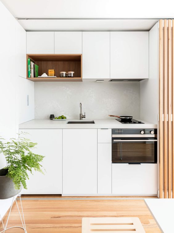 A small, minimalist kitchen in white with a white tile backsplash and a white stone worktop that can be hidden with a privacy screen