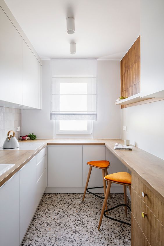 a small, minimalist kitchen with sleek white cabinets, butcher block countertops, and a bar counter for cooking and dining