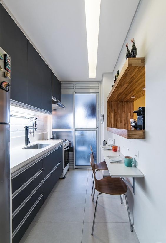 a small, elegant black kitchen with a thick white stone countertop, a white tile backsplash, a built-in shelf with a coffee machine and a bar table