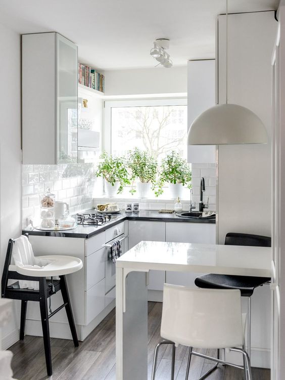 a small Scandinavian kitchen with glossy white cabinets, black countertops, a bar countertop, a pendant lamp and stools