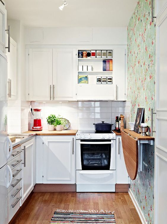 a small white kitchen with a white thin tile backsplash, a floral wallpaper wall, a folding table and a printed rug