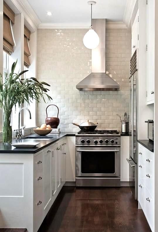 a small white kitchen with black countertops, a white glazed tile backsplash, parasols, a green vase and hanging lamps