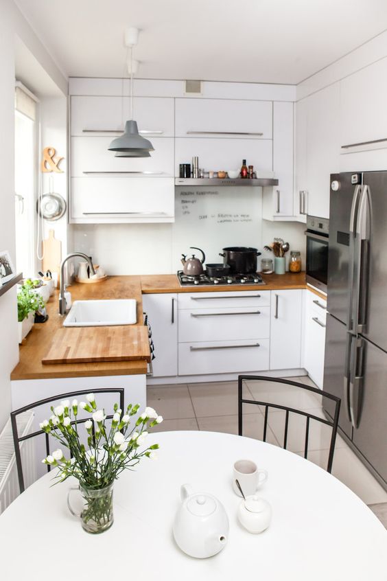 a small white kitchen with butcher block countertops, stainless steel appliances, and a round table and chairs