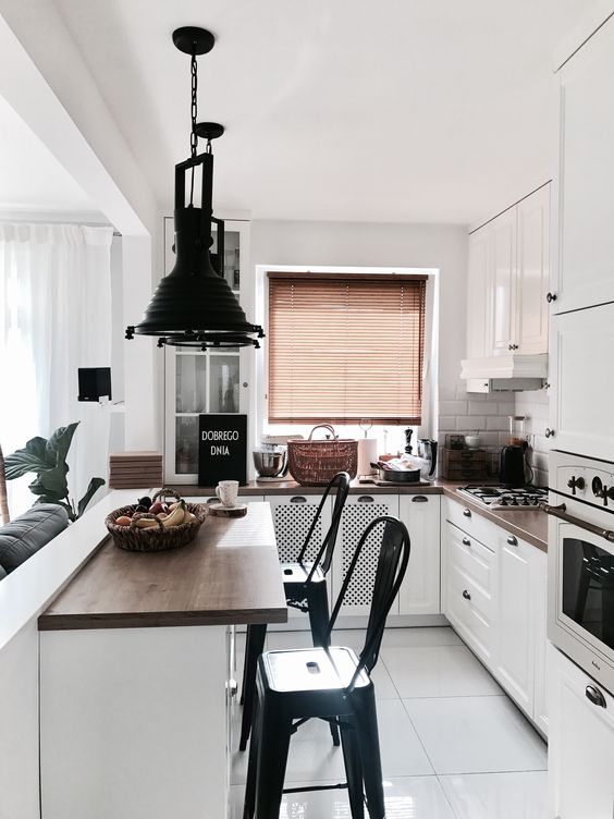 a small white kitchen with dark stained countertops, white tiles on the back wall, dark pendant lamps and black stools