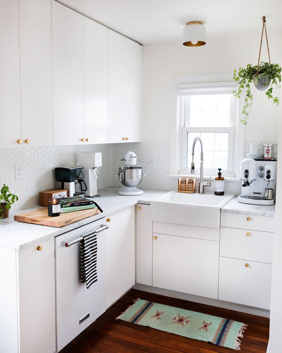 a small white kitchen with penny tiles, white stone countertops, gold knobs and potted plants