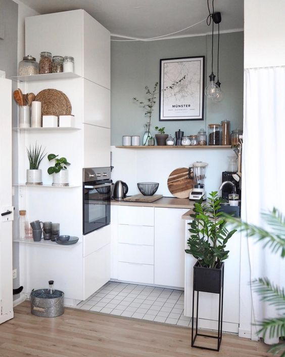a small Scandinavian kitchen with elegant white cabinets, some open shelving and built-in appliances, as well as hanging lamps