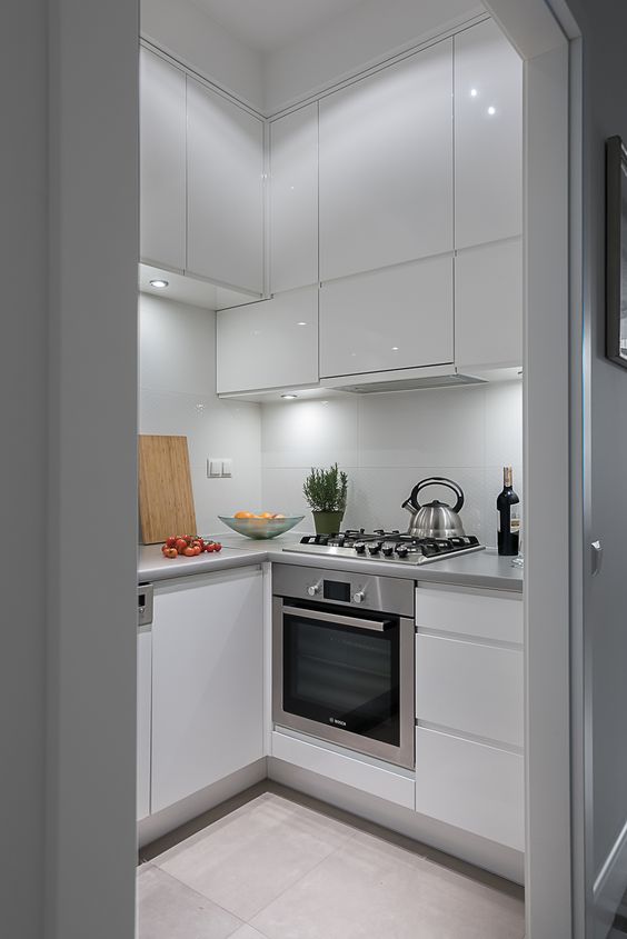 A tiny white sleek kitchen with built-in lighting, metal countertops, and built-in appliances is chic and cool