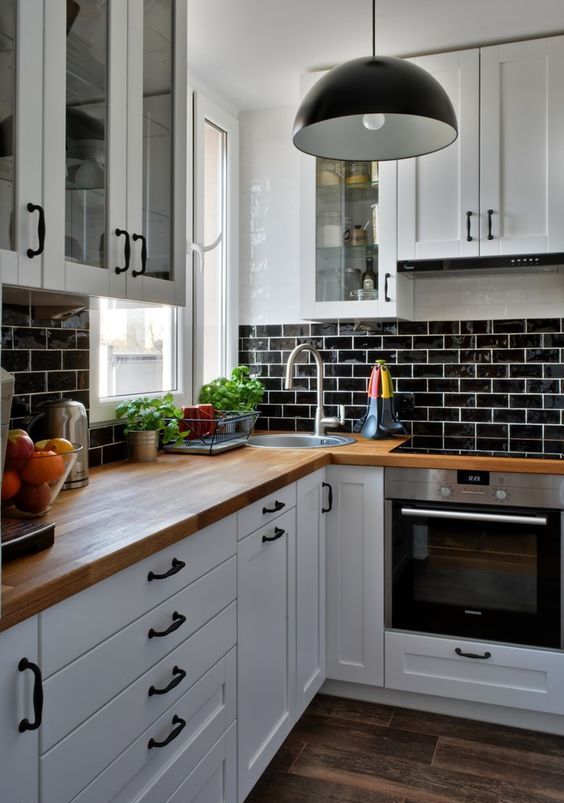 a white farmhouse kitchen with black glazed tiles, butcher block countertops and black pendant lamps
