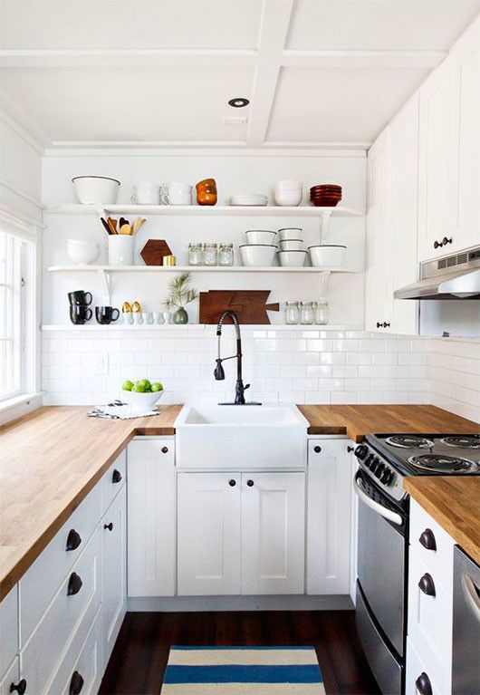a white farmhouse kitchen with butcher block countertops, open shelving, and black handles and knobs